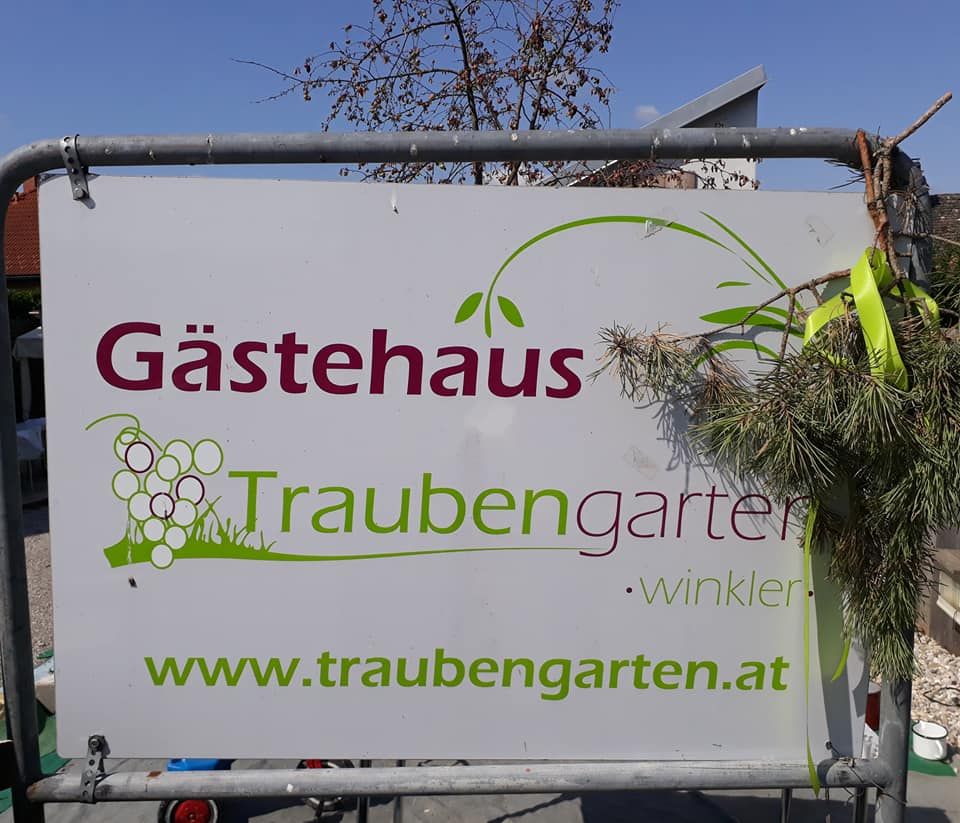 Sign with the inscription 'Gästehaus Traubengarten Winkler' and website address, decorated with branches.