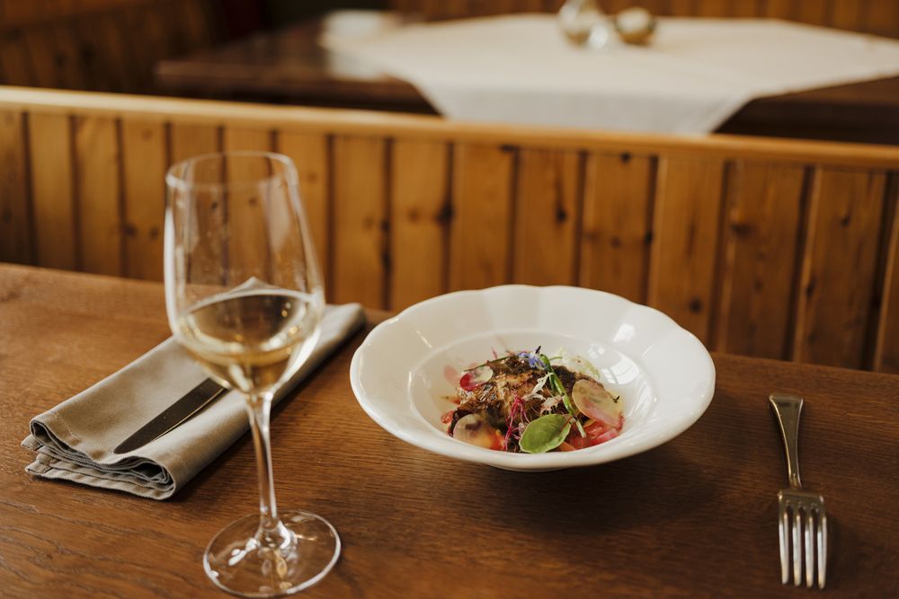 A glass of white wine next to a plate with a decorative dish on a wooden table.