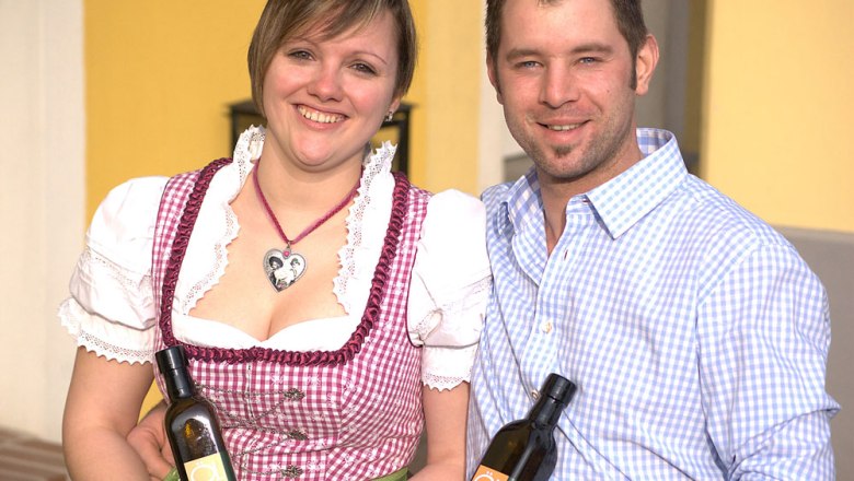 A smiling couple holds bottles of oil in their hands.