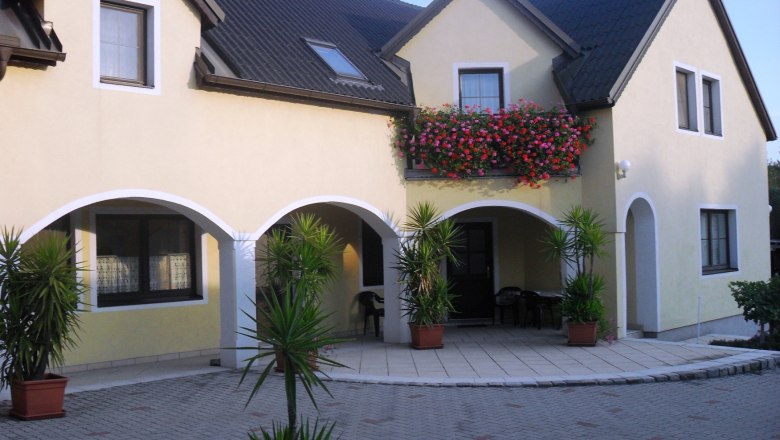 yard, © Berthold A yellow house with a dark roof, a balcony with flowers and plants in the courtyard.