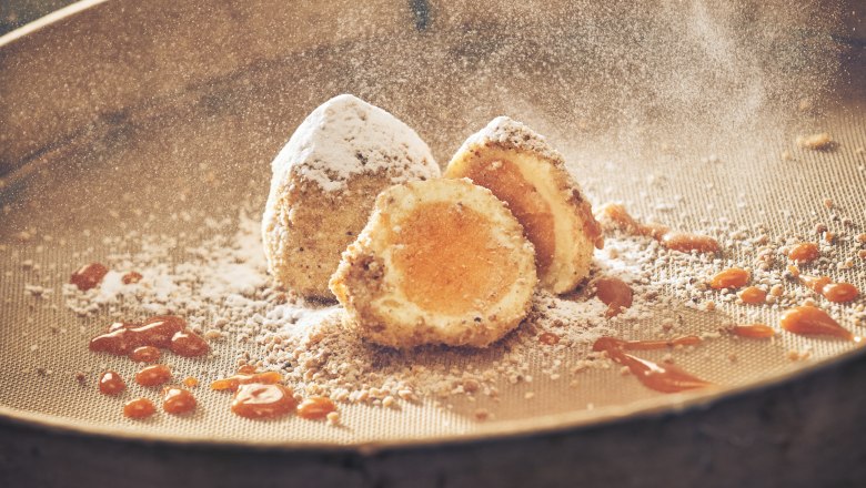 Iced apricot dumplings with powdered sugar and apricot sauce on a sieve.