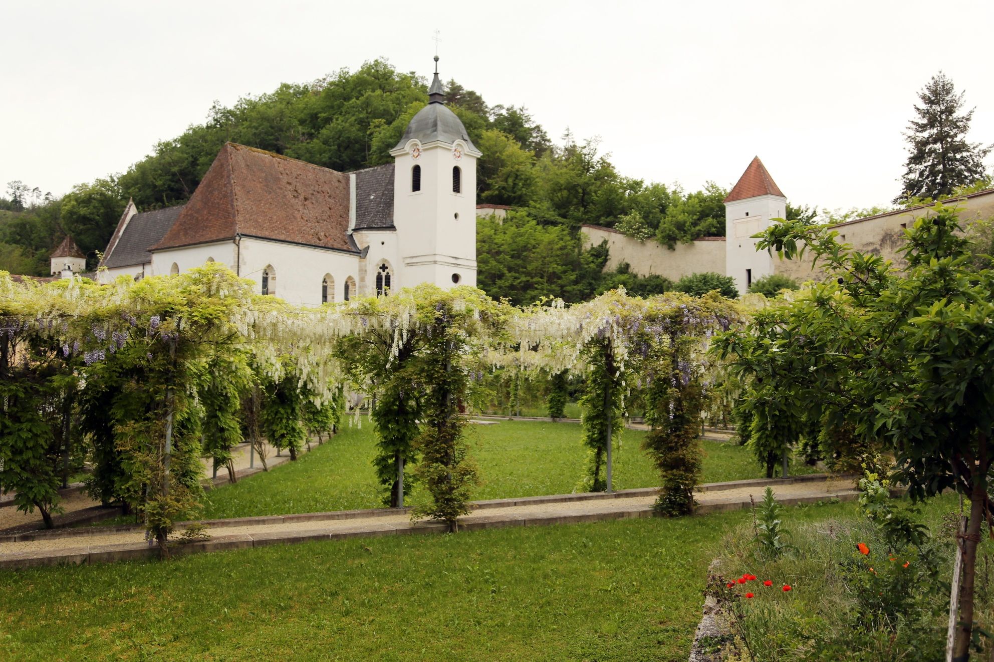 View of a historic charterhouse with garden and pergola.