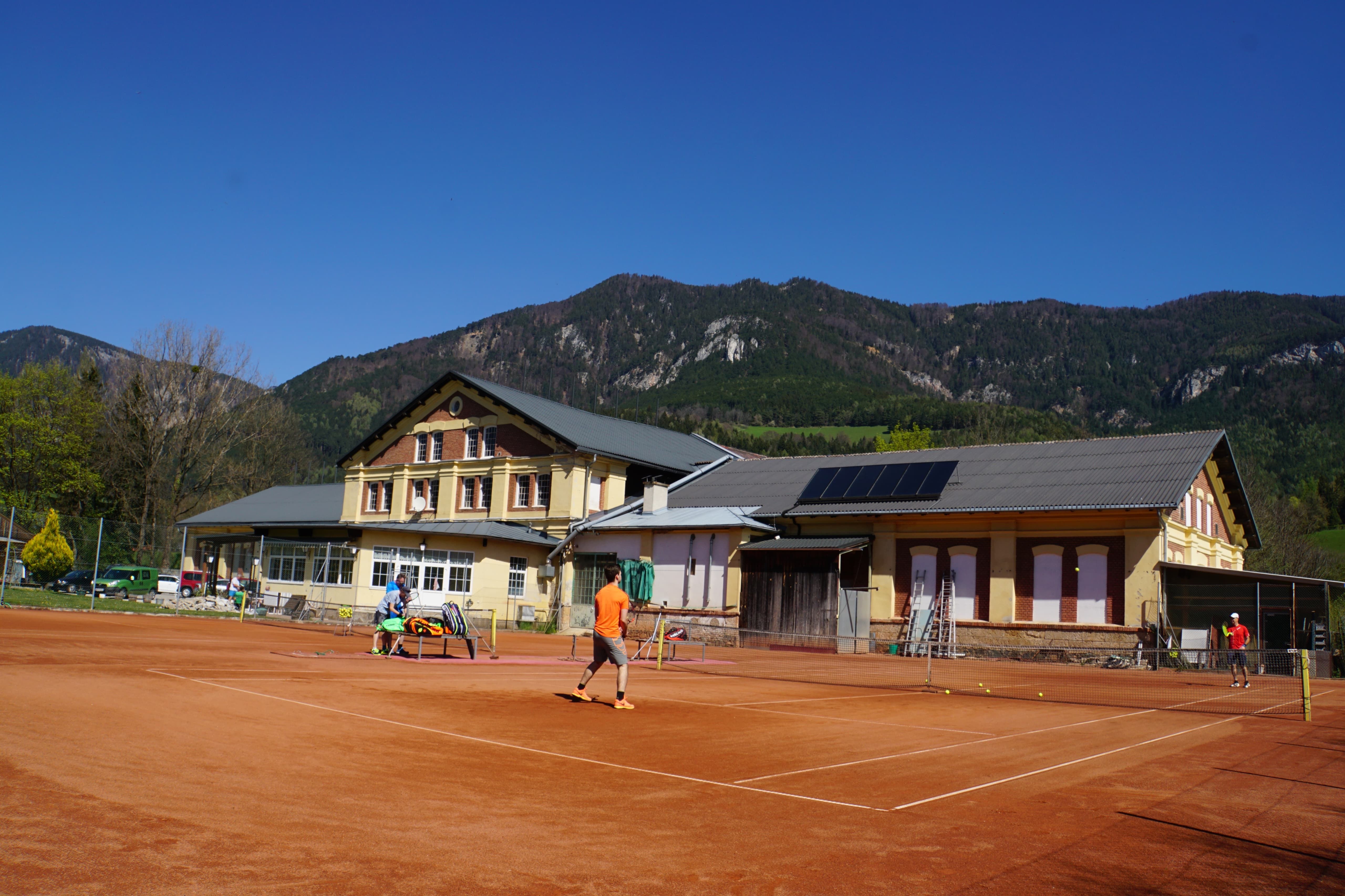 Tennis court in front of a building with mountains in the background.