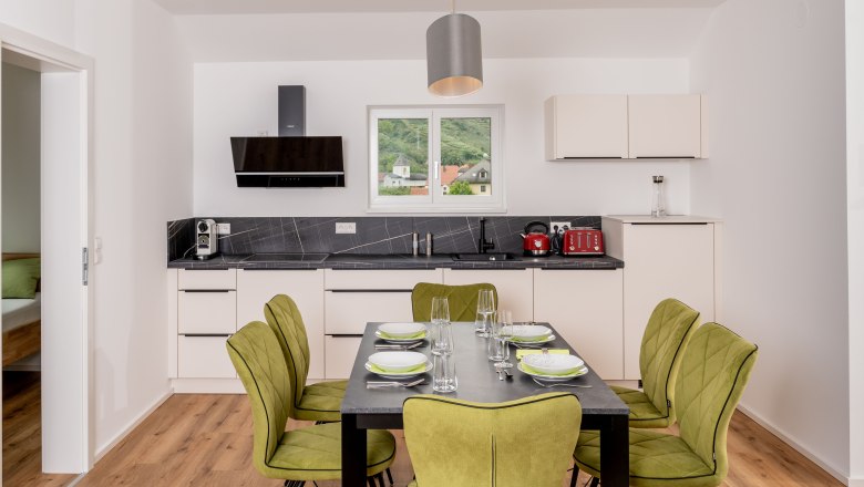 Modern kitchen with dining table and green chairs, window with view of the hills.