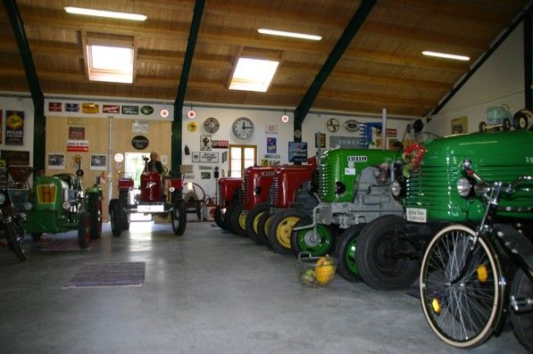 Interior view of a barn with several vintage tractors in different colors, surrounded by retro advertising signs on the walls.