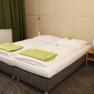 Comfortable hotel room with double bed, green towels and bedside table with flowers and fruit.