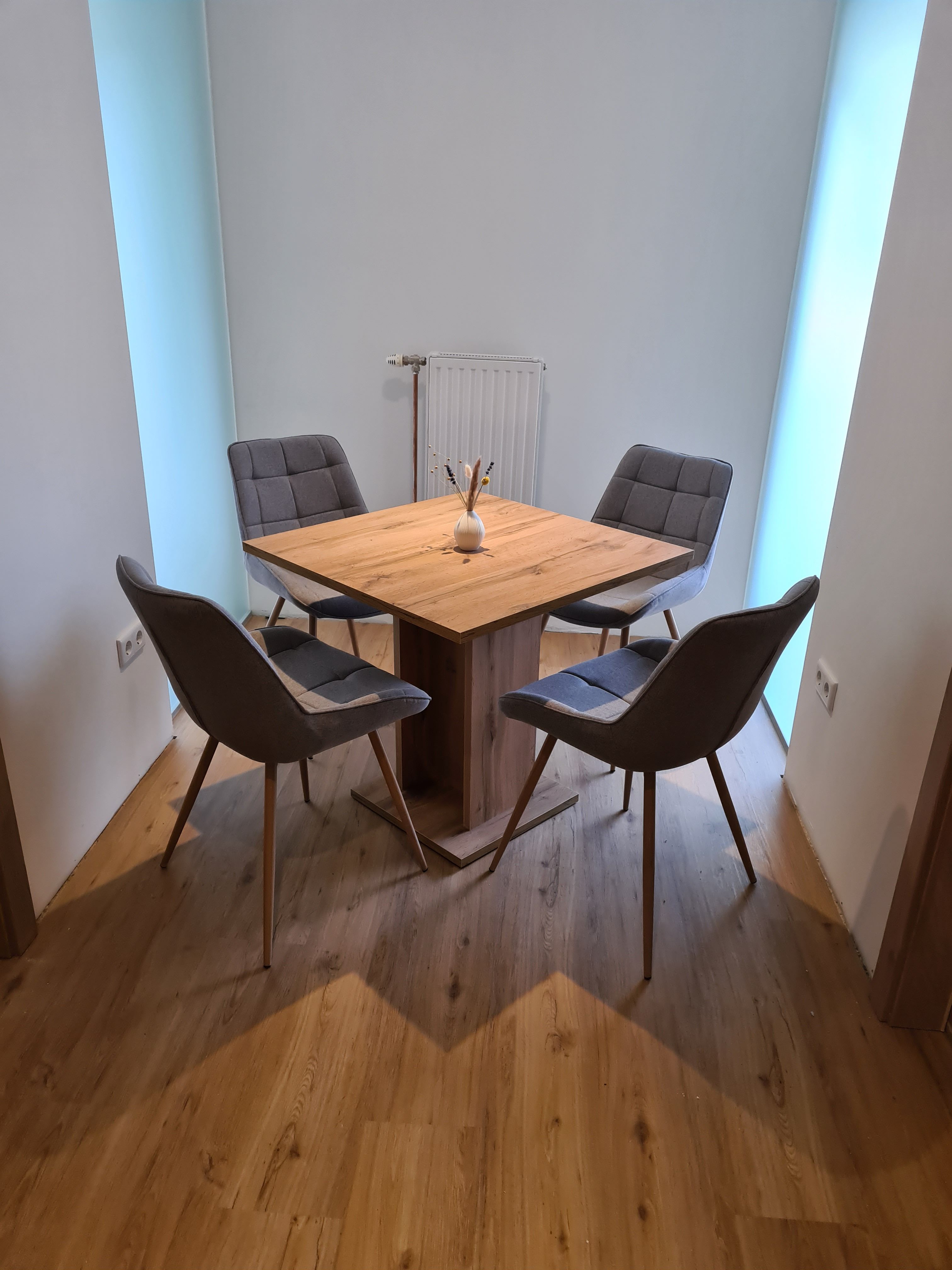 A modern dining table with four gray chairs in a bright room.
