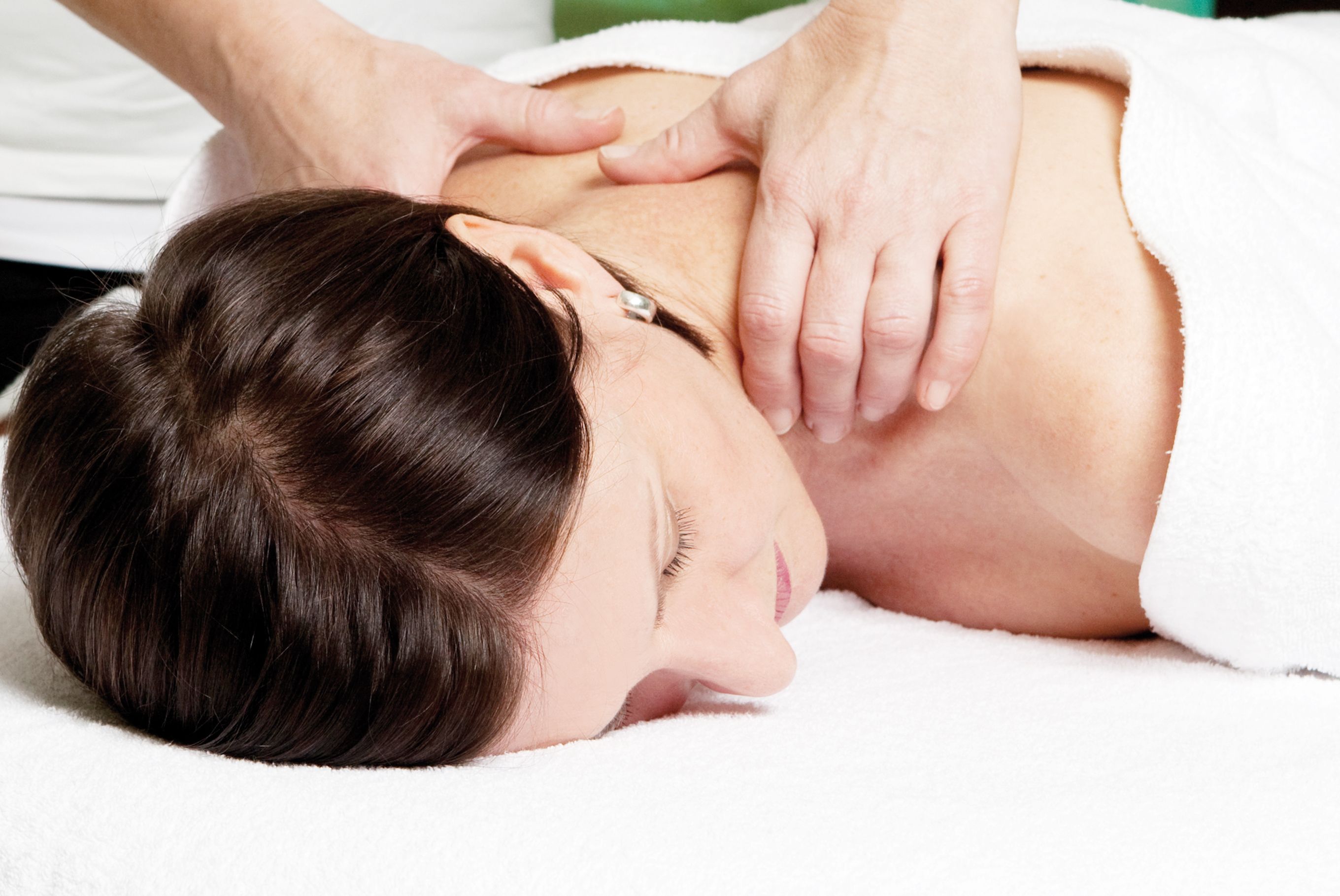 A woman receives a neck massage while lying on a white towel.