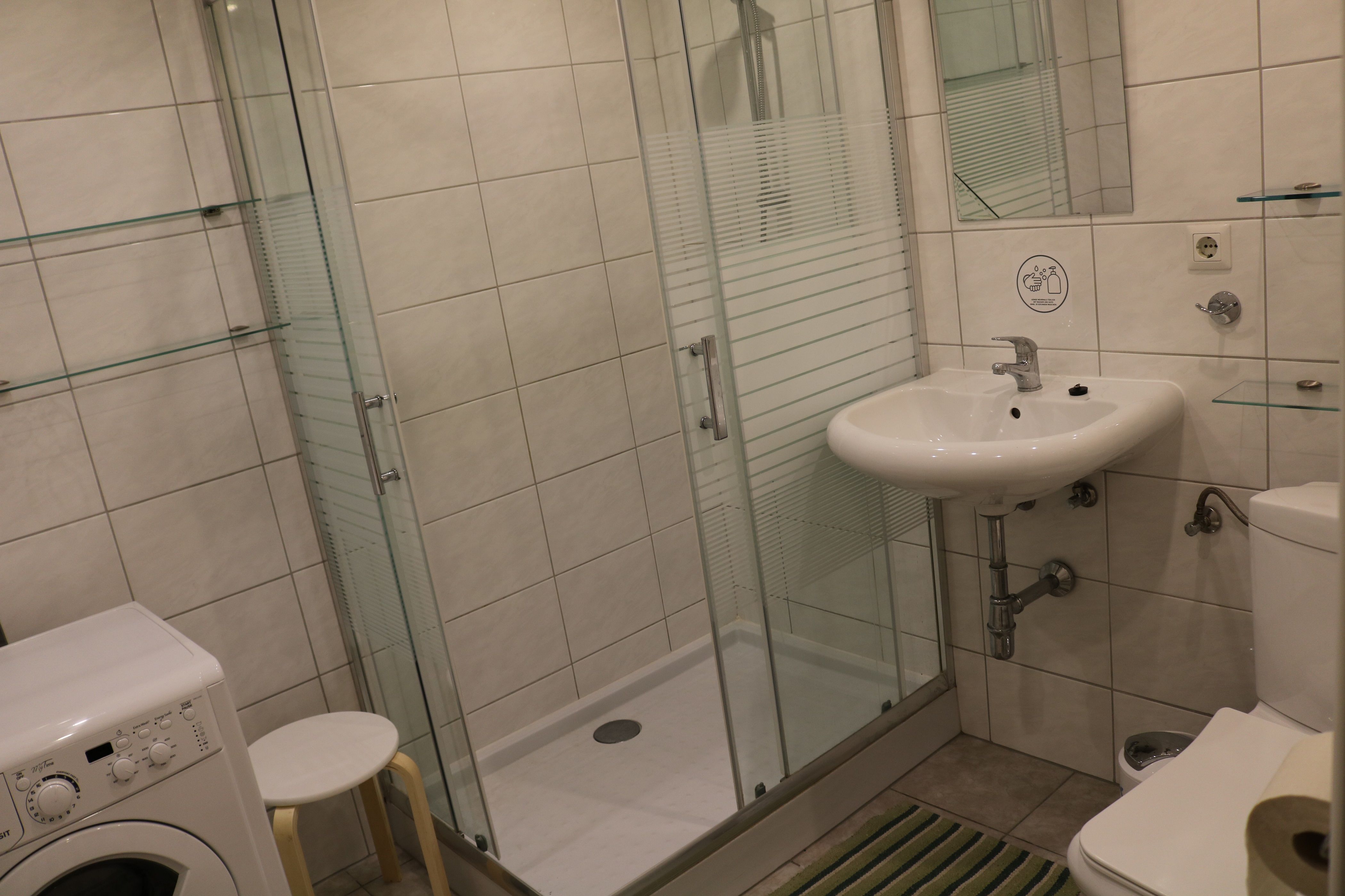 Modern bathroom with shower, washbasin, toilet and washing machine.