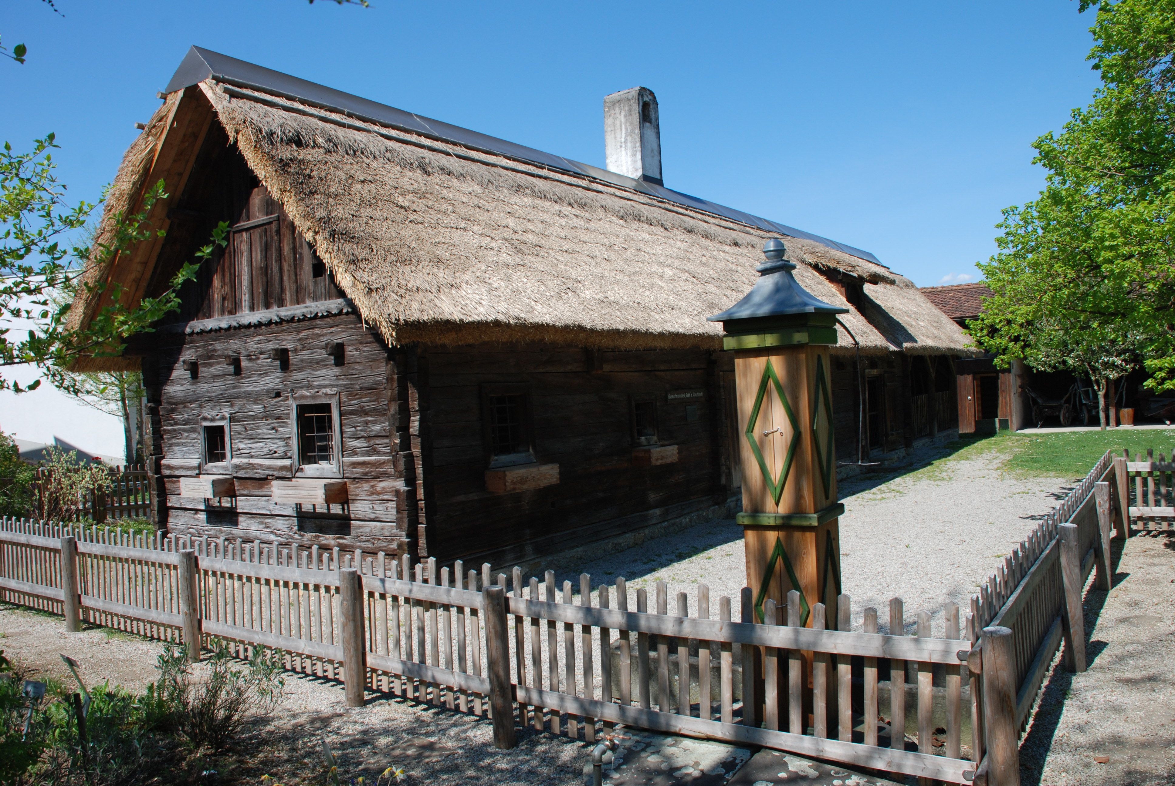 Traditional wooden house with thatched roof and wooden fence in a rural setting.