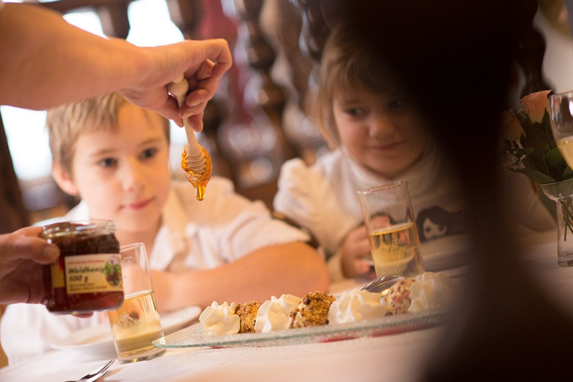 Two children watch as honey is drizzled on a dessert.