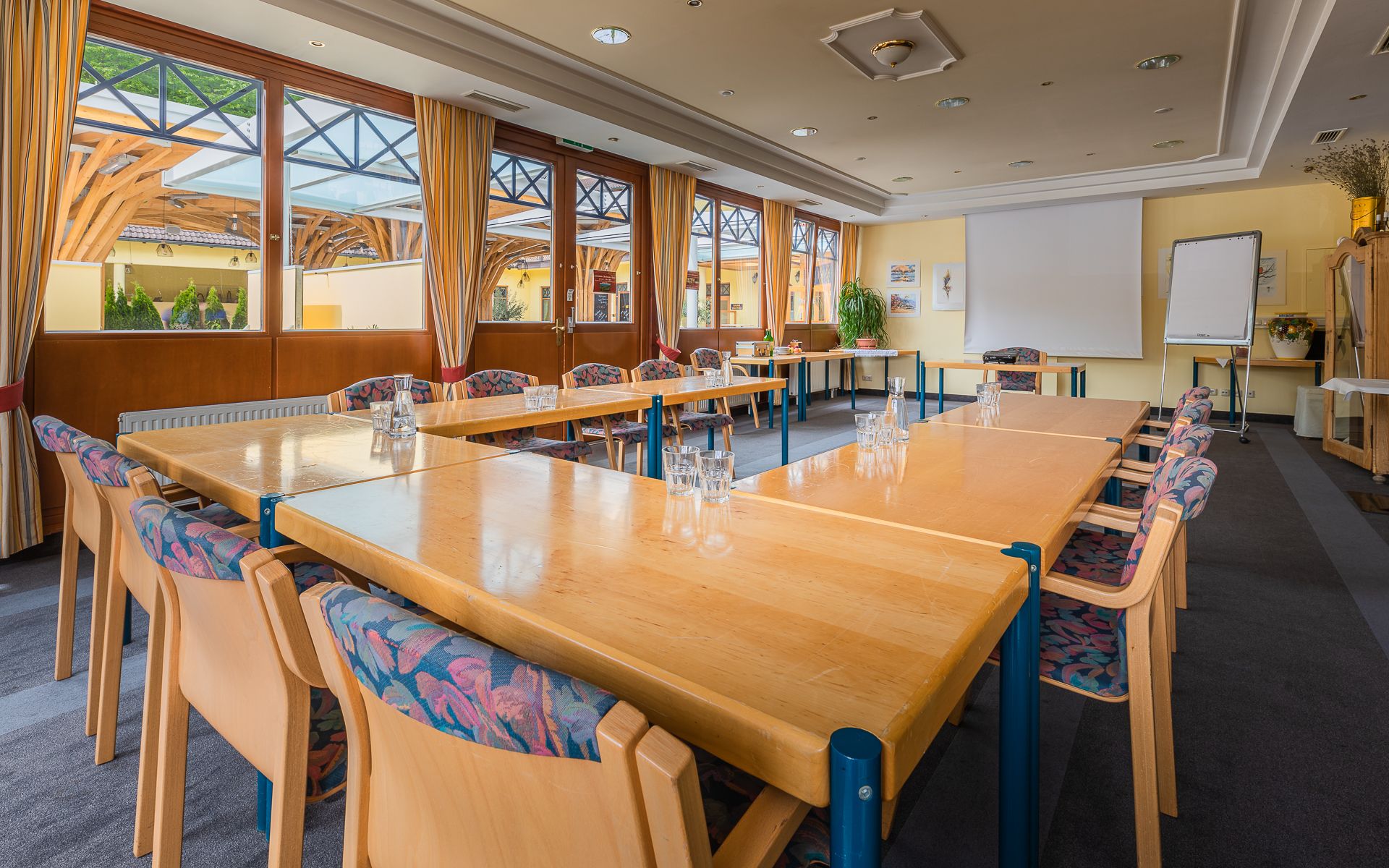 A bright seminar room with large windows, U-shaped tables, chairs and a flipchart.