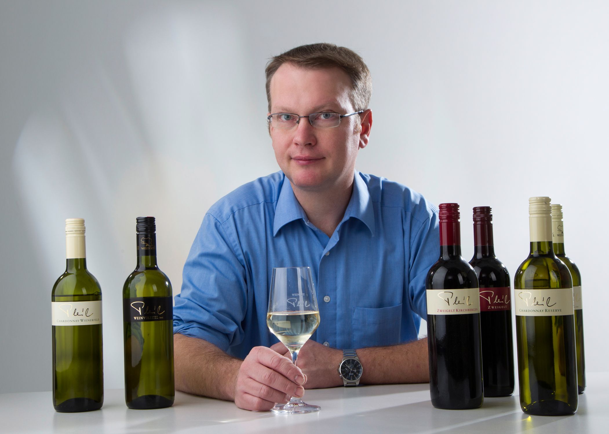 Man in blue shirt with wine glass and wine bottles on a table.