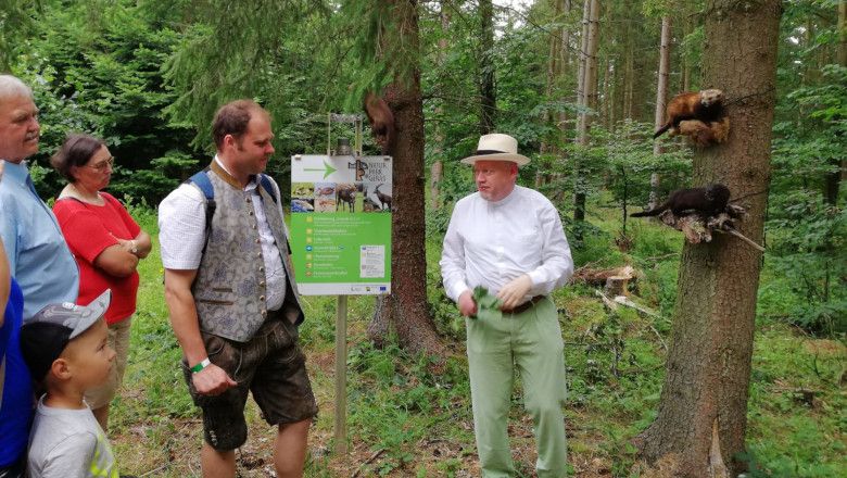 Group of people in the forest listening to a man standing in front of a sign in Geras Nature Park.