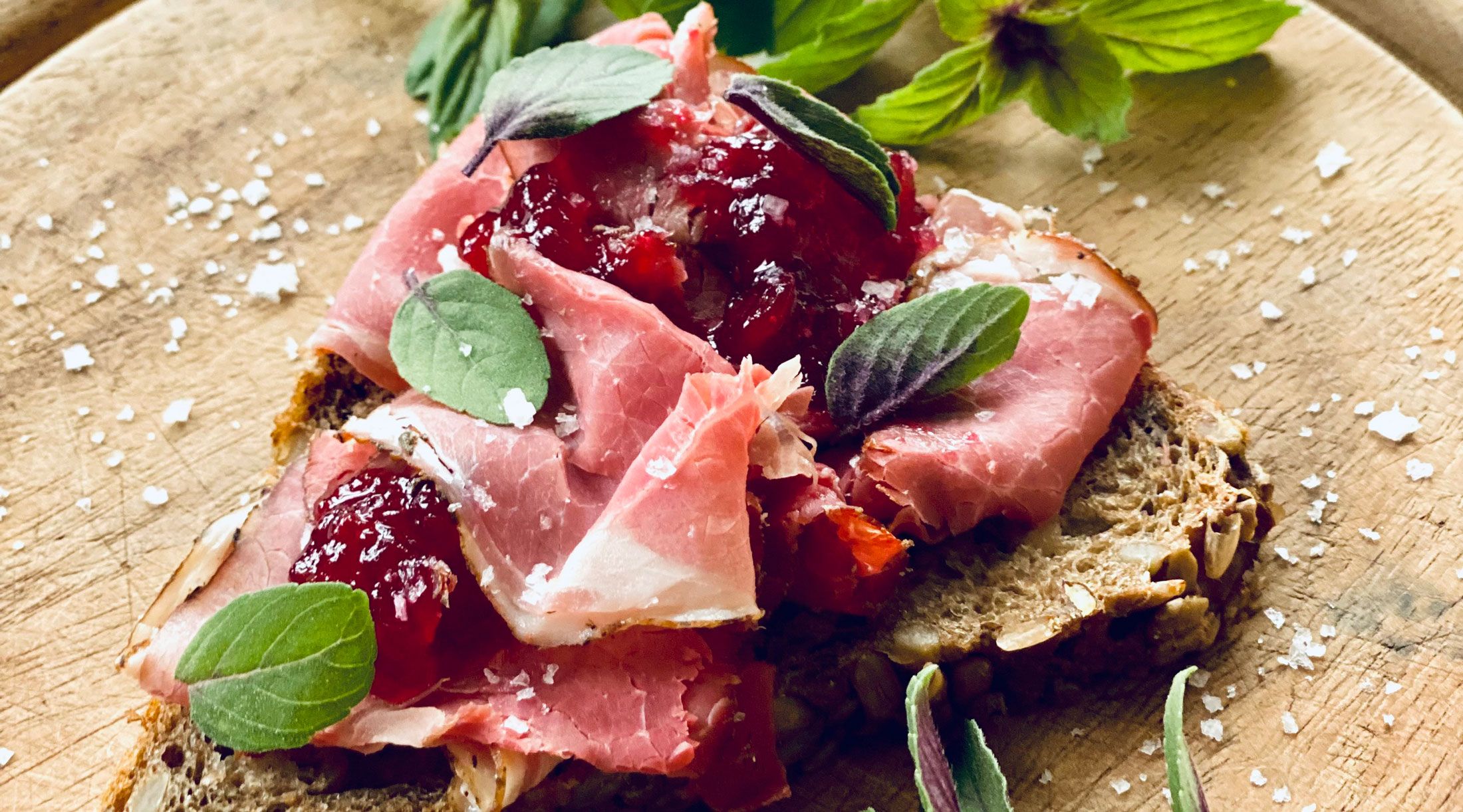 Close-up of a sandwich with ham, cranberries and herbs on a wooden board.