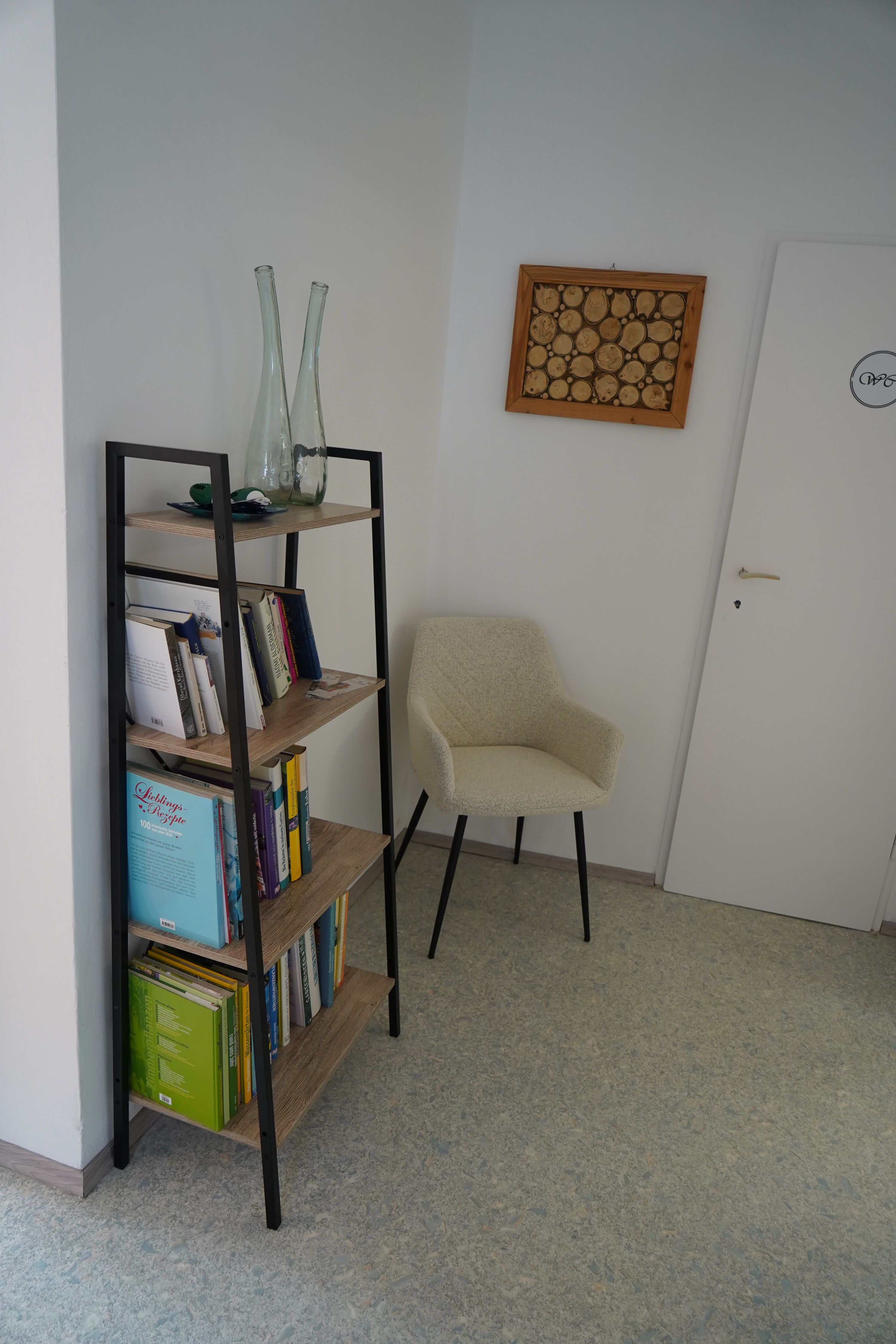 A bookshelf with books and decorations, a beige chair next to it and a door in a room.