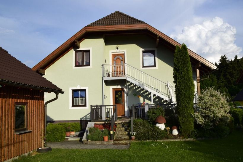 A two-story house painted green with an outdoor staircase in the garden.
