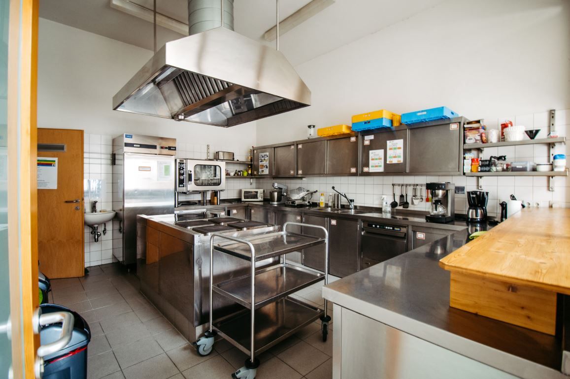 Modern canteen kitchen with stainless steel appliances and work surfaces.