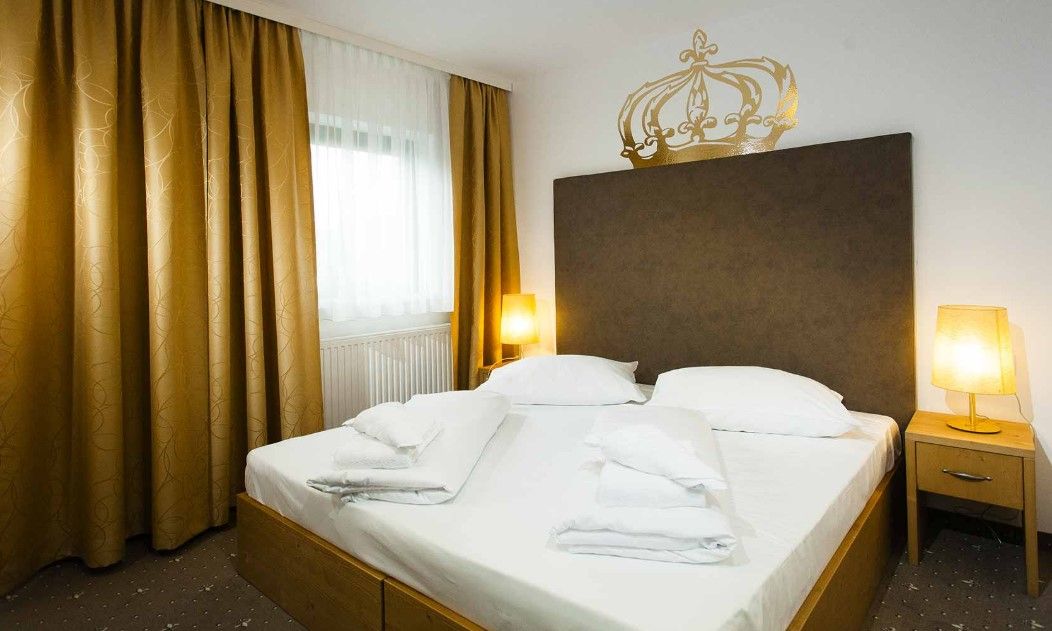 A double room with a large bed, golden curtains and two bedside tables with lamps.