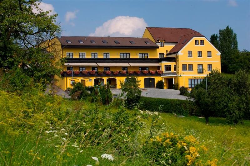 Yellow hotel building with flower balconies, surrounded by green landscape.