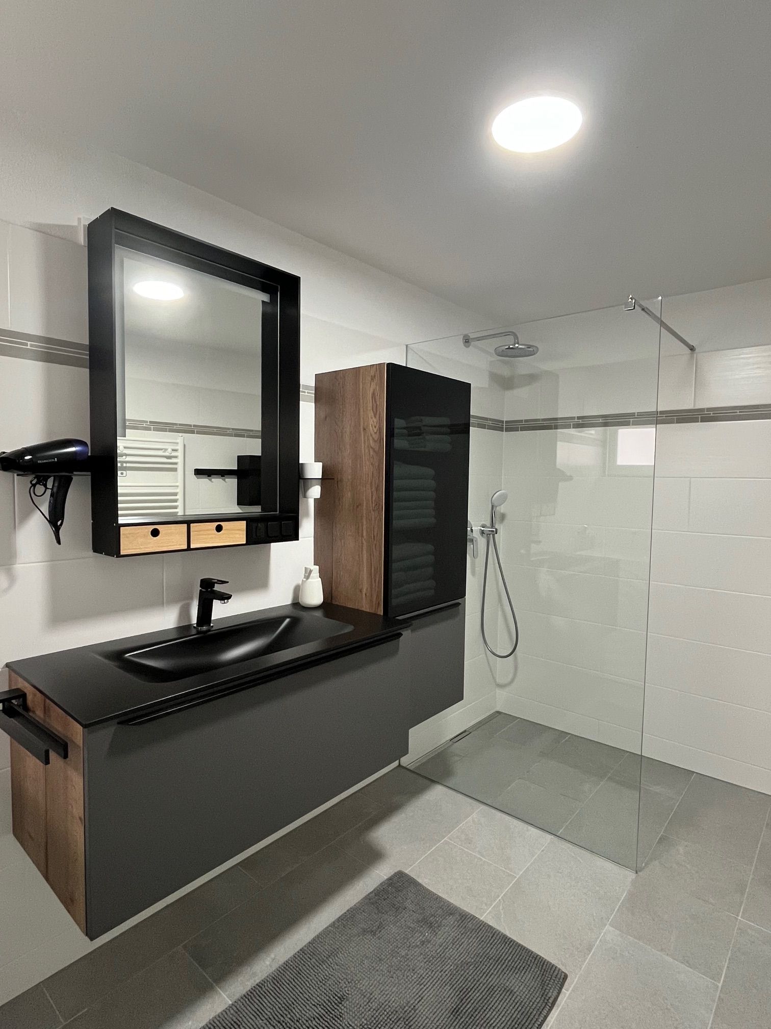 Modern bathroom with black washbasin, mirror, rain shower and gray tiles.