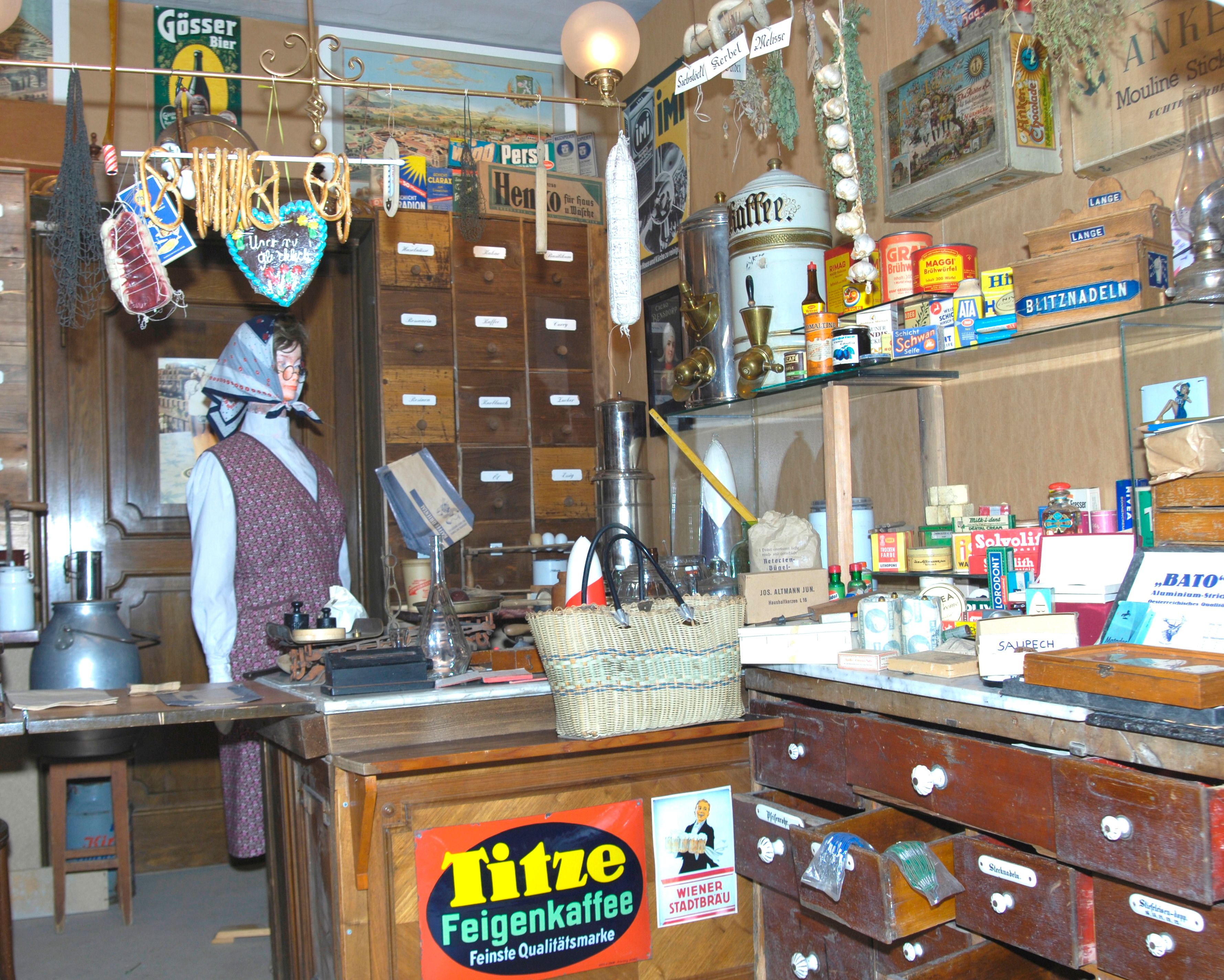 Interior view of a historic merchant's store with shelves full of old products and a mannequin in traditional clothing.