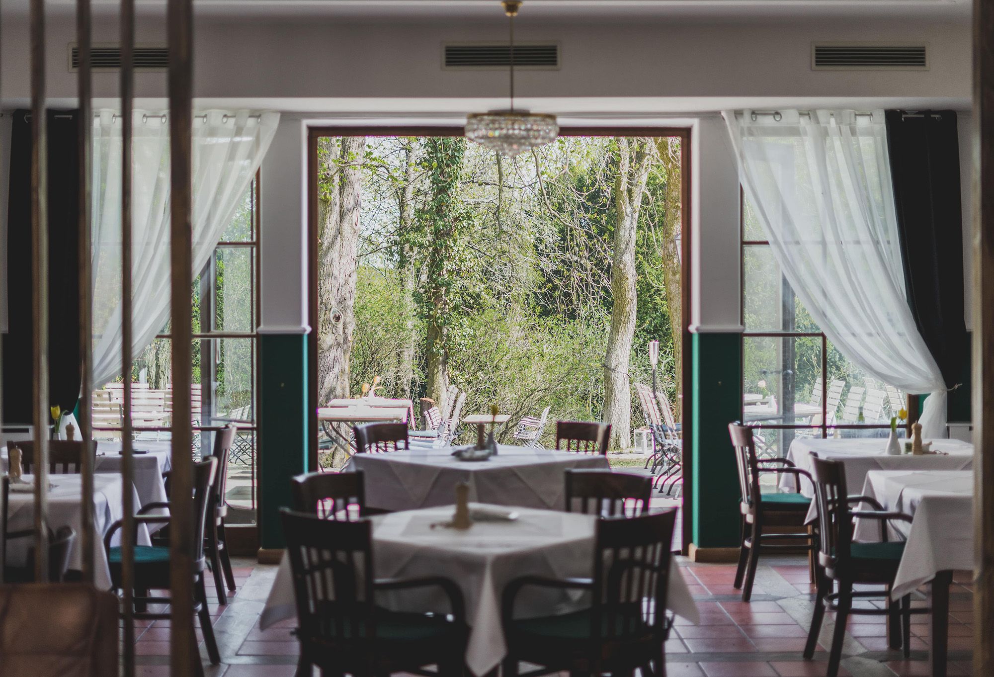 A restaurant with set tables and a view of a green garden through large windows.