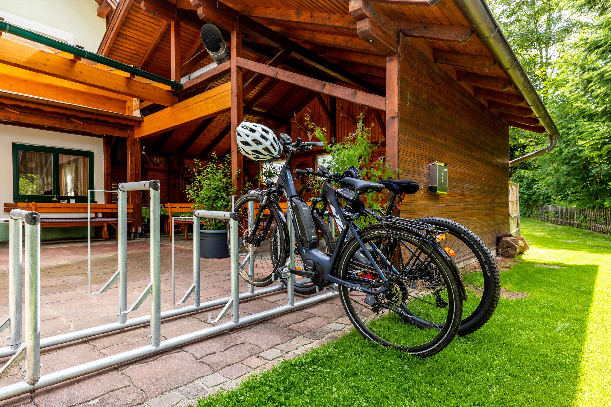 Bicycles in a bicycle rack in front of a wooden building with a terrace.