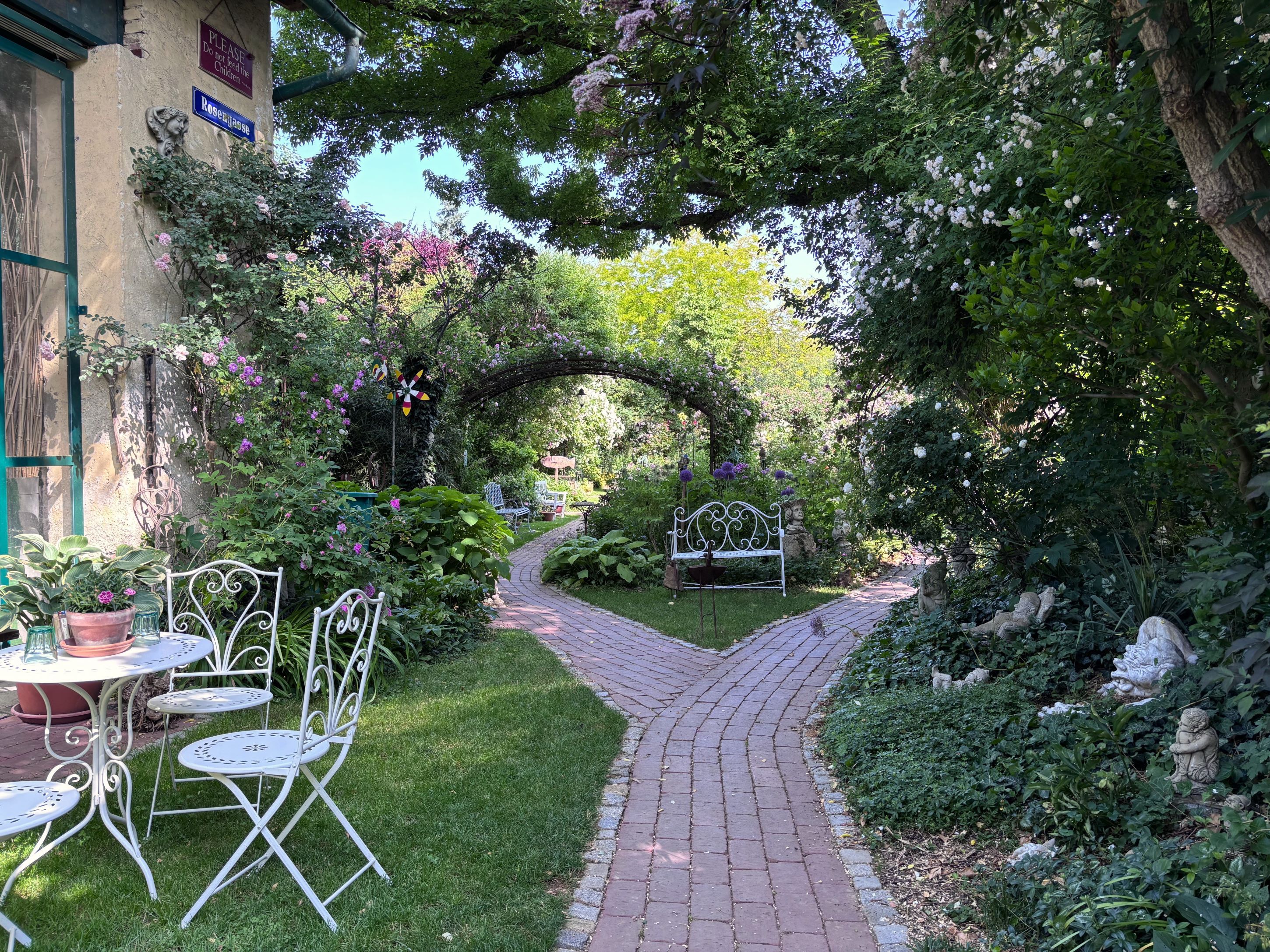 An idyllic garden with white garden furniture, a paved path and lush vegetation.