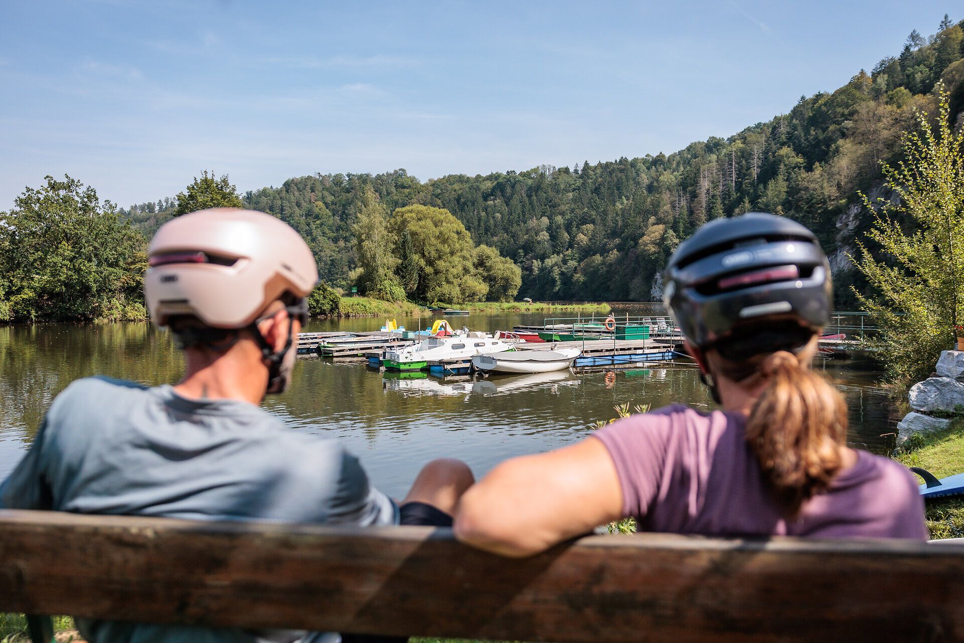 The gentle breeze caresses the glistening reservoir while cyclists relax on a bench and enjoy the picturesque landscape. Surrounded by lush greenery and rolling hills, this place invites you to unwind and experience the beauty of nature.