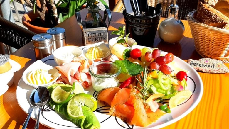 A breakfast plate with salmon, cold cuts, fruit and butter on an outdoor table.