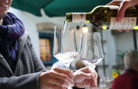 Wine is poured into a glass while one person holds it.