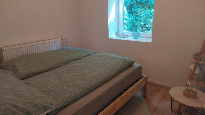 A cozy bedroom with a bed, a window with a view of the greenery and a picture on the wall.
