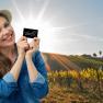 Woman with hat holding VinoQ card in front of a sunny vineyard.