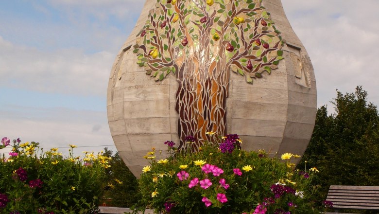 Large concrete bulb with leaf inscription 'Gsundheit sollst lebn' and flowers in the foreground.