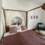 Cozy bedroom with four-poster bed, pillows, books and an armchair with rabbit cushions.