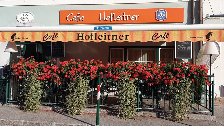 Exterior view of Café Hofleitner with red flowers and awning.