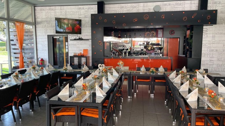 A stylishly furnished café with laid tables and a bar in the background.