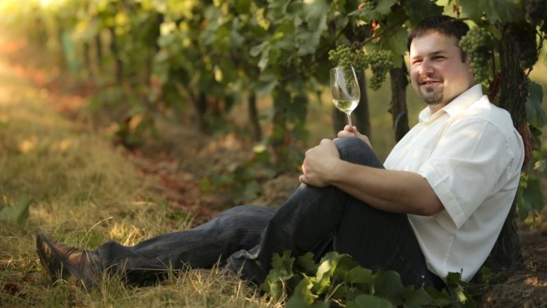 Man sitting in the vineyard with a glass of white wine.