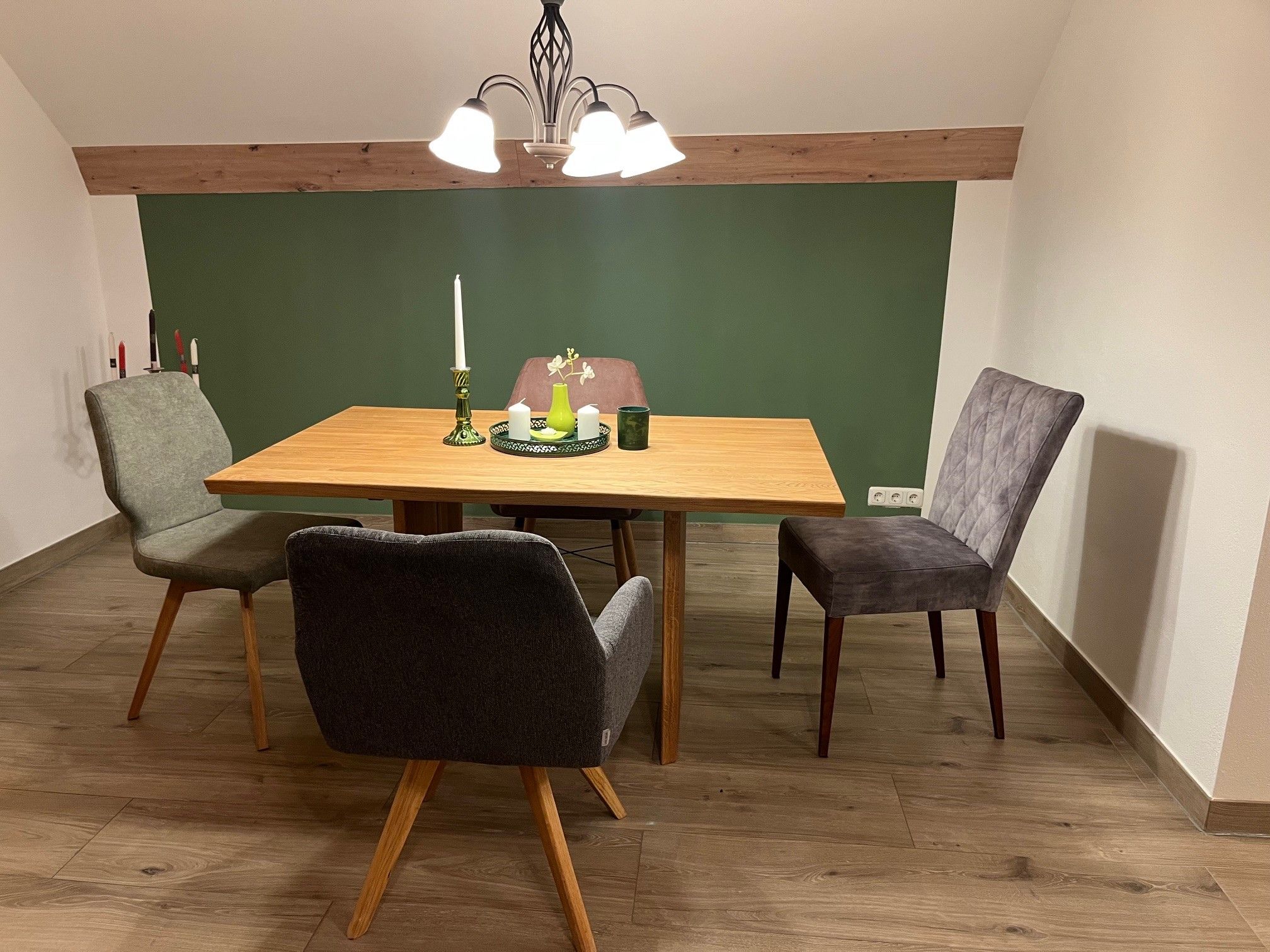 A dining table with four chairs in a room with a green accent wall and wooden floor.
