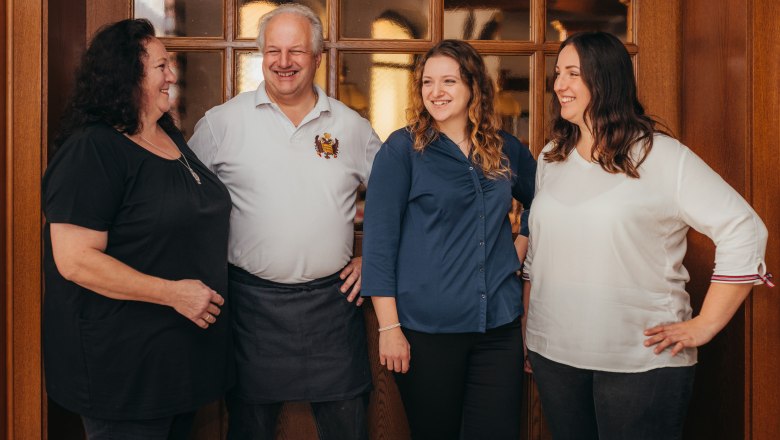 Four people smile in front of a wooden door in an interior room.