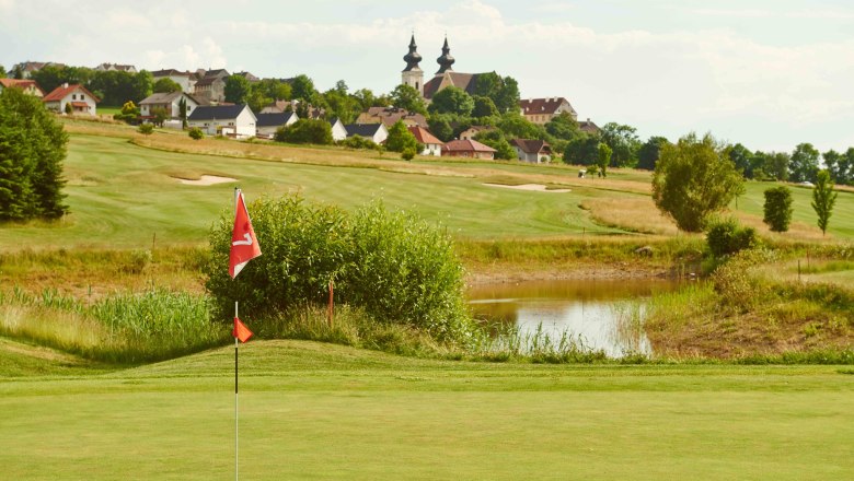 Golf course with flag in the foreground, village and church in the background.