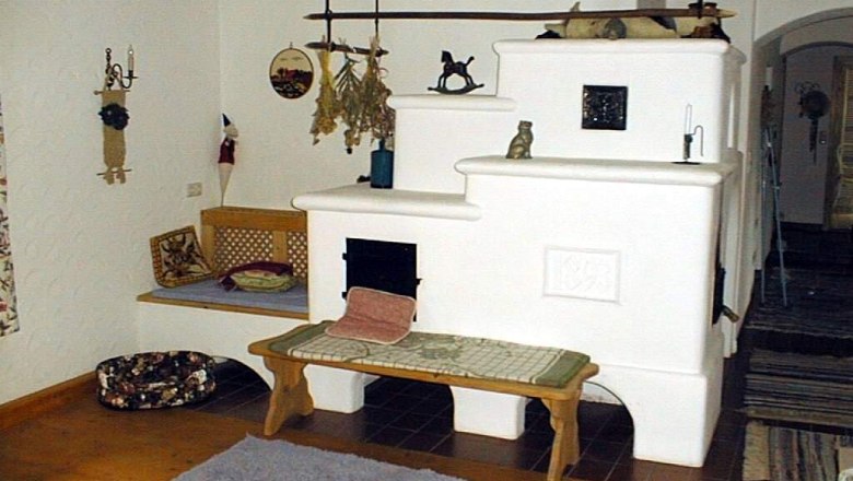 Cozy room with white tiled stove and wooden beams.