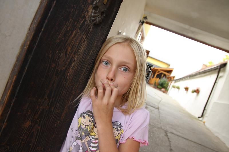 A girl stands in an archway and looks at the camera in surprise.