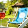 A glass with a red drink and a straw on a deckchair in the garden.