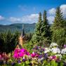 Church tower surrounded by trees and flowers in front of a mountain landscape.