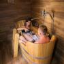 A couple relaxes in a wooden hot tub with wine in a rustic room.