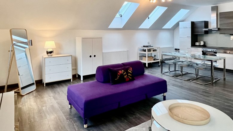 Modern loft with purple sofa, dining table and kitchen under skylights.