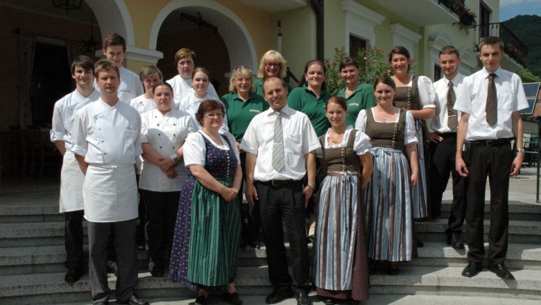 A group of people in work clothes stand in front of a building with arches.