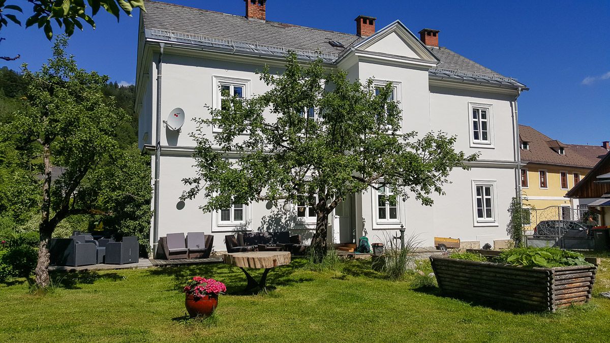 A white two-story house with a garden and trees.